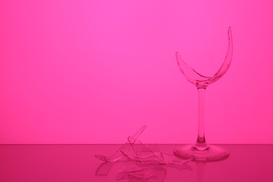 Photo of Pieces of broken wine glass against magenta background, space for text. Color tone effect