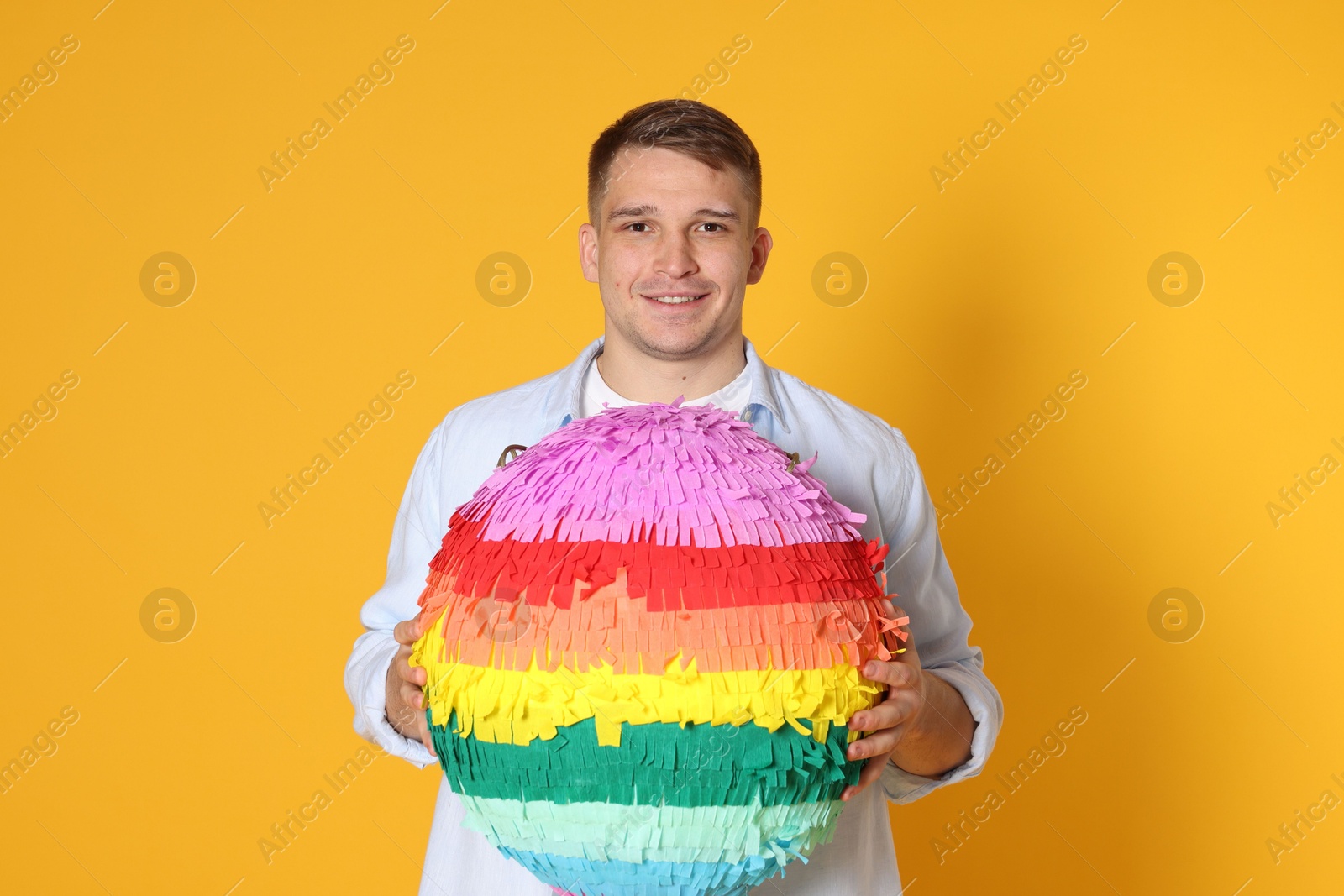 Photo of Happy man with colorful pinata on yellow background