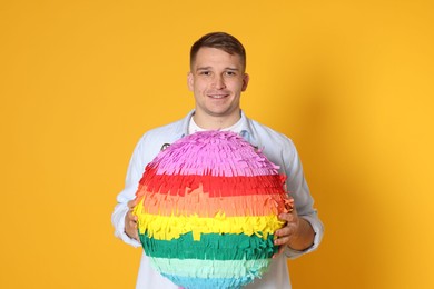 Photo of Happy man with colorful pinata on yellow background