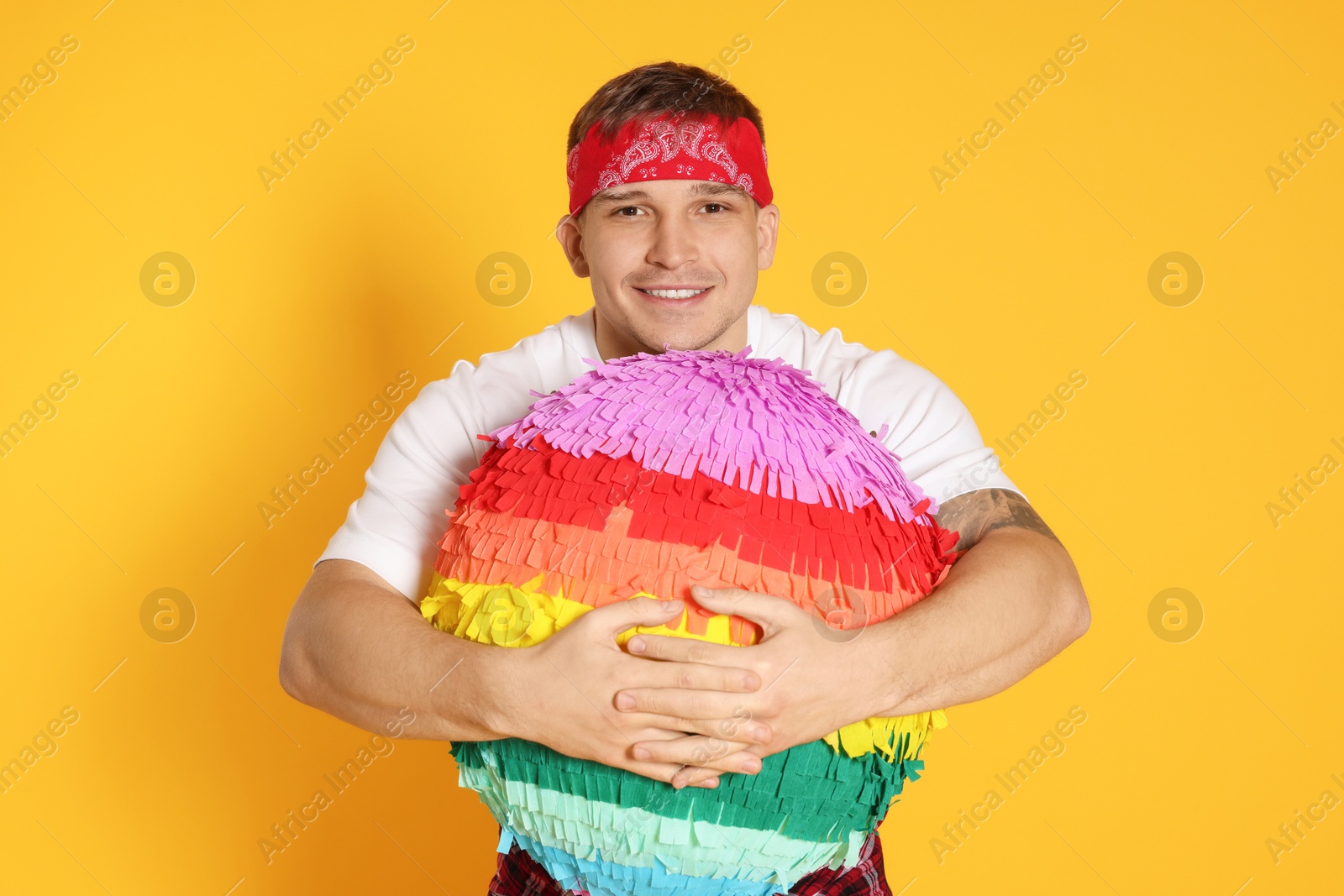 Photo of Happy man with colorful pinata on yellow background