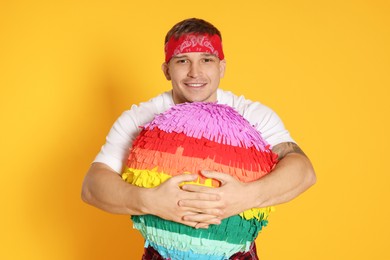 Photo of Happy man with colorful pinata on yellow background