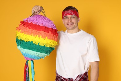 Photo of Happy man with colorful pinata on yellow background