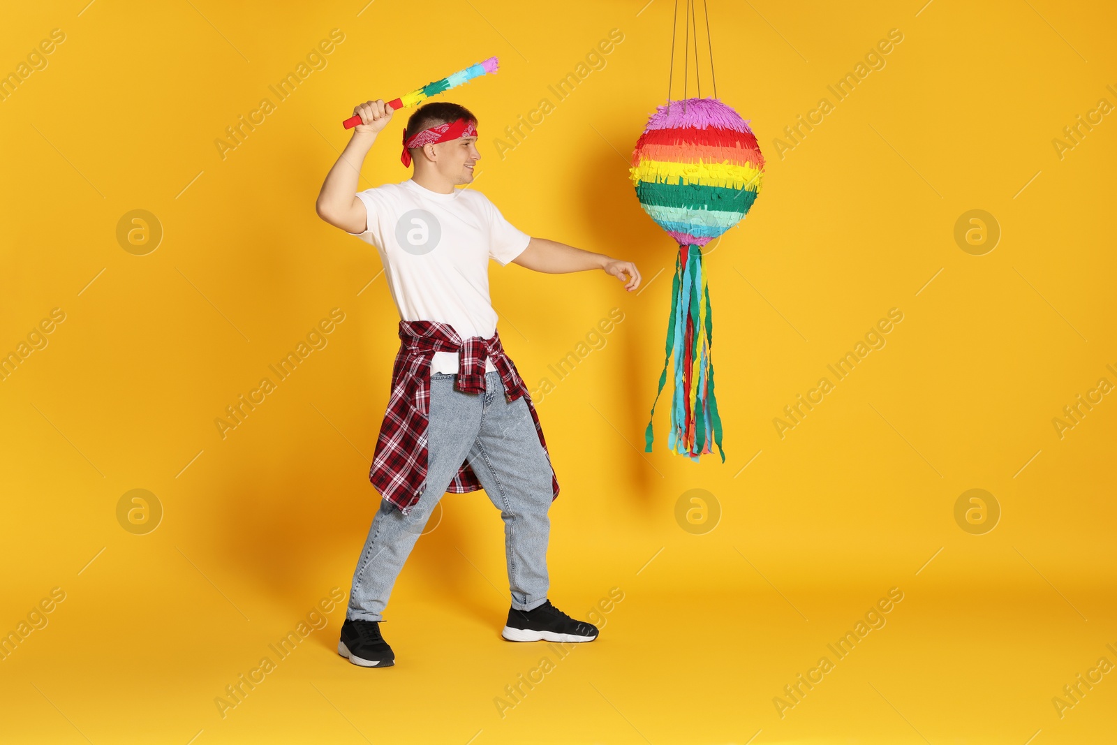 Photo of Happy man breaking pinata on yellow background