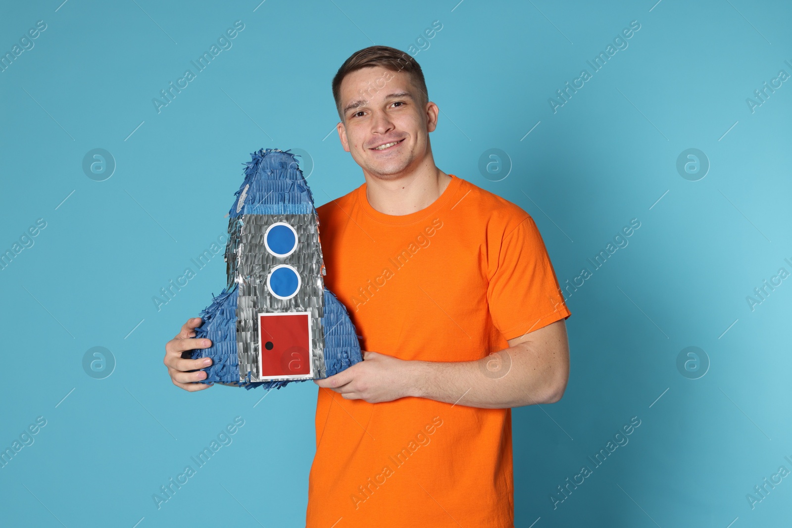 Photo of Happy man with pinata in shape of spaceship on light blue background