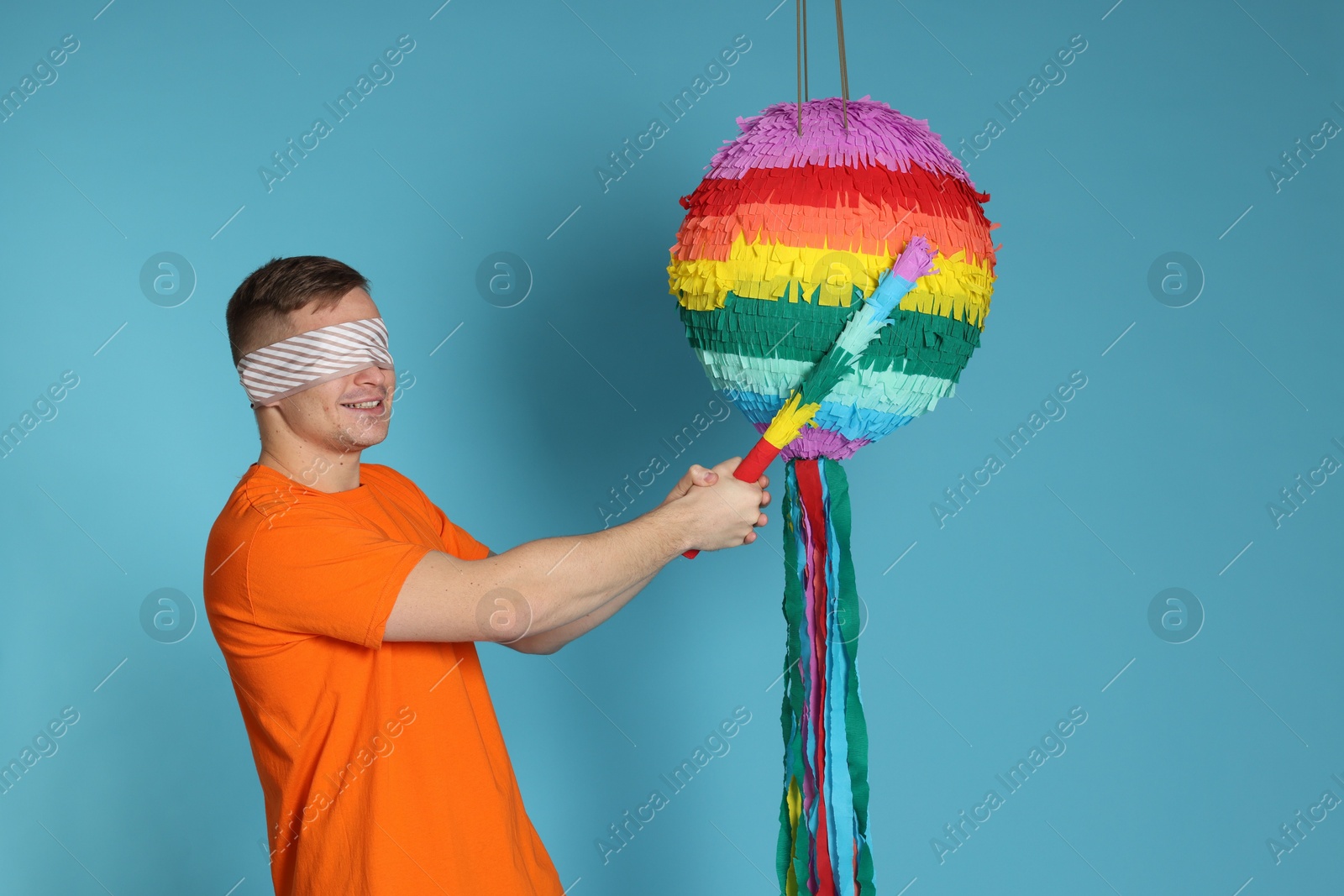 Photo of Man with tied eyes breaking pinata on light blue background