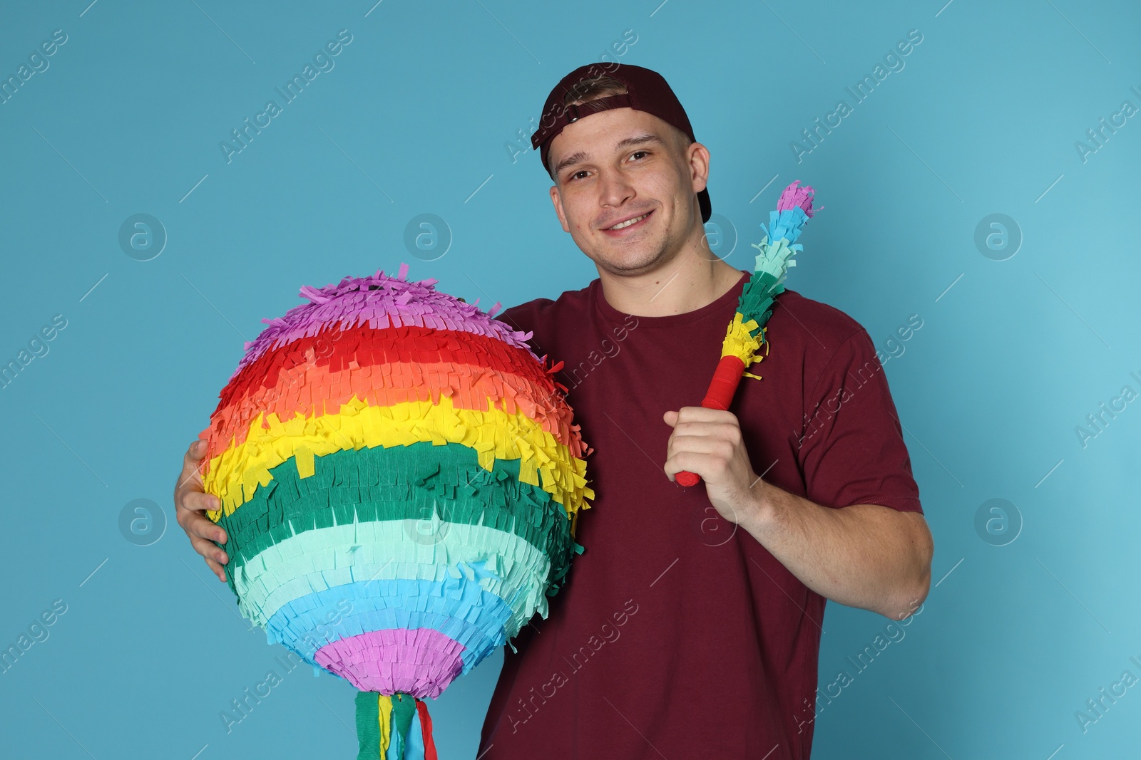 Photo of Happy man with colorful pinata and stick on light blue background