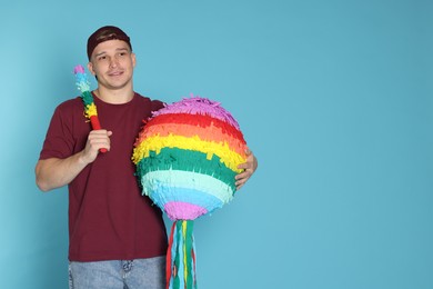 Photo of Happy man with colorful pinata and stick on light blue background. Space for text