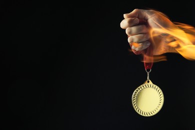 Image of Woman holding gold medal in her flaming hand on black background, closeup. Space for text