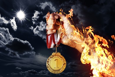 Image of Woman holding gold medal in her flaming hand against darkened sky, closeup