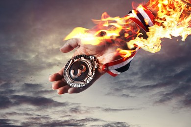 Image of Woman holding bronze medal in her flaming hand against sky, closeup