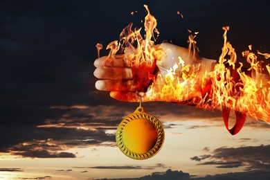 Image of Woman holding gold medal in her flaming hand against darkened sky, closeup