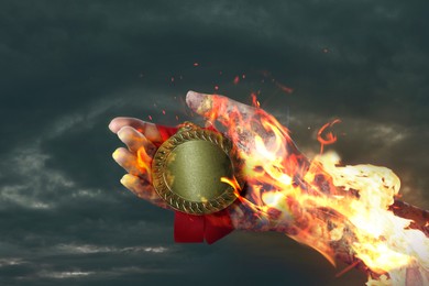 Image of Woman holding gold medal in her flaming hand against darkened sky, closeup