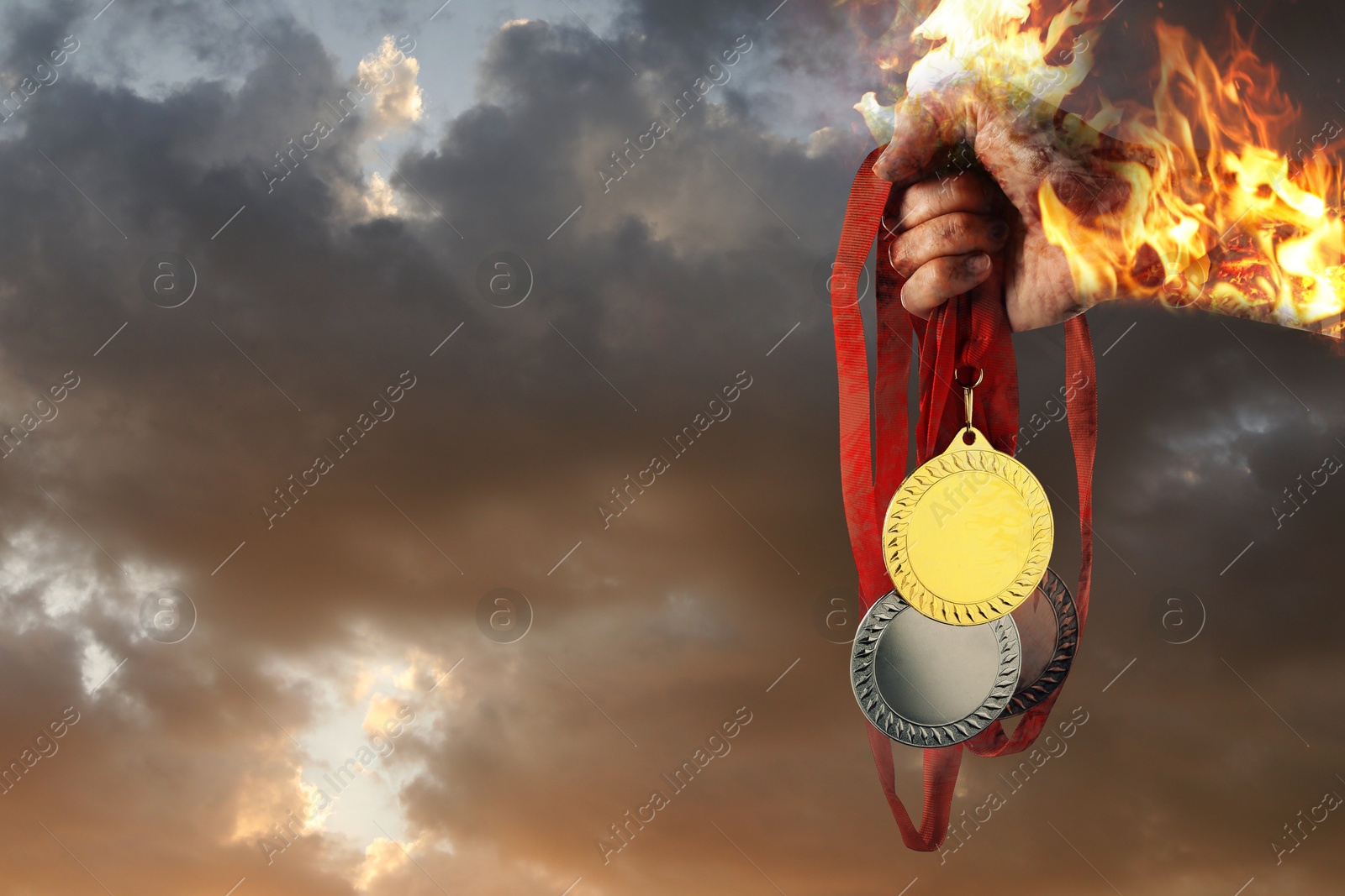 Image of Woman holding gold, silver and bronze medals in her flaming hand against sunset sky, closeup