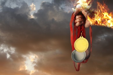 Image of Woman holding gold, silver and bronze medals in her flaming hand against sunset sky, closeup