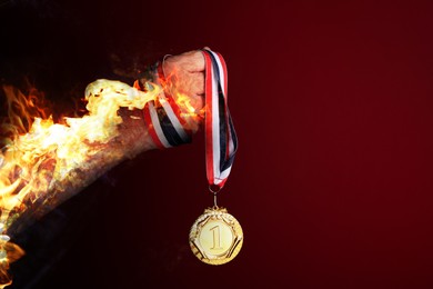 Image of Man holding gold medal in his flaming hand on red background, closeup