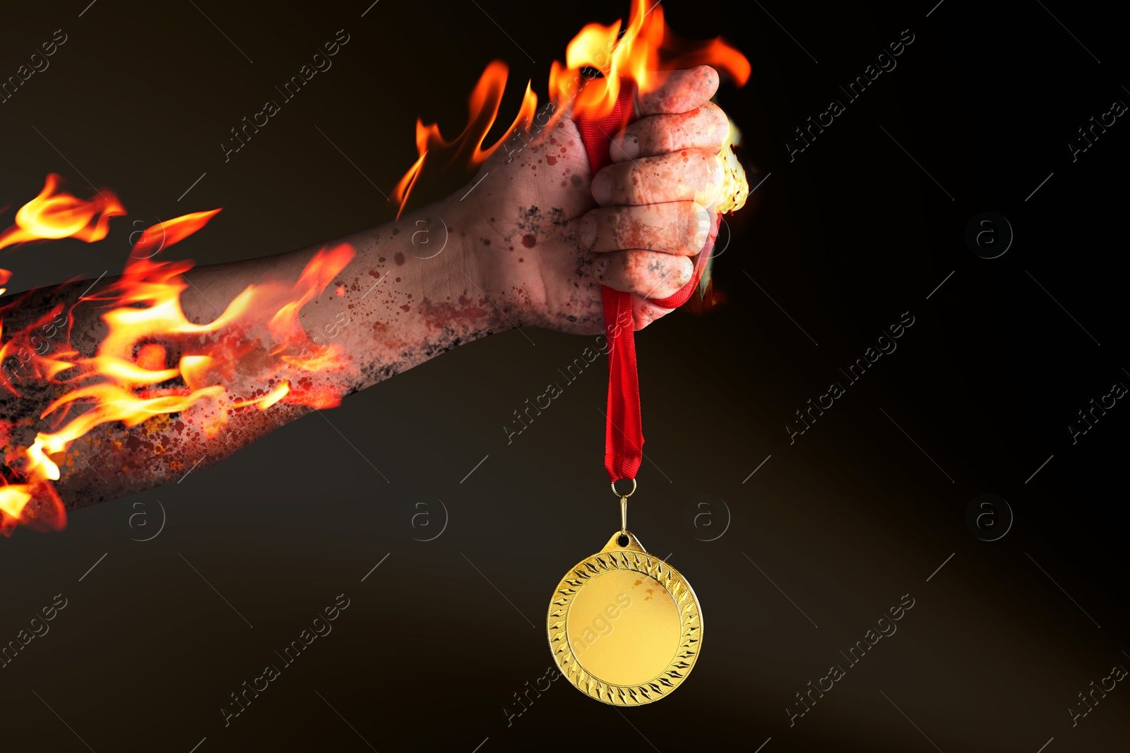 Image of Man holding gold medal in his flaming hand on black background, closeup