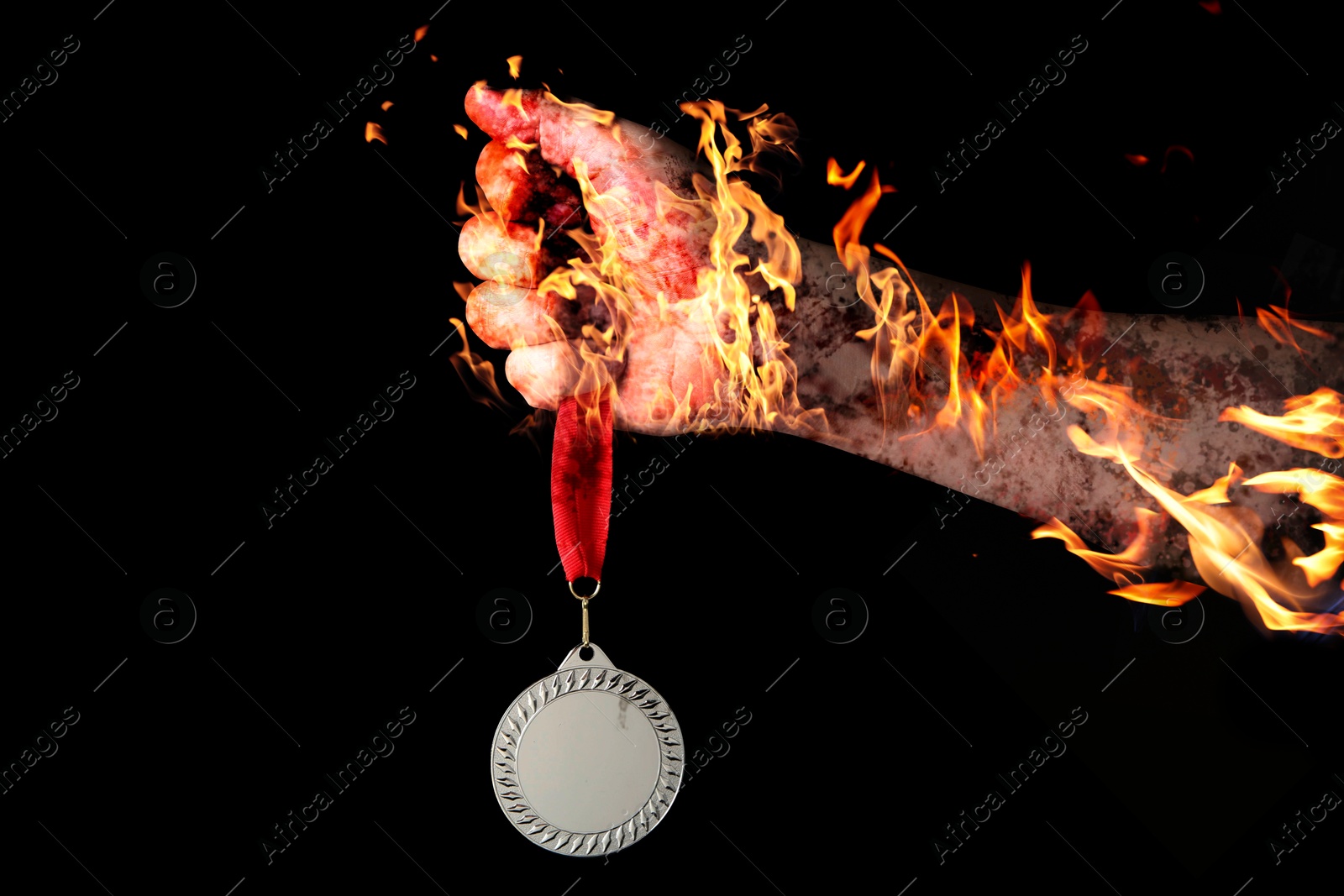 Image of Man holding silver medal in his flaming hand on black background, closeup