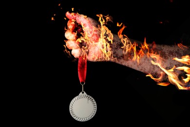 Image of Man holding silver medal in his flaming hand on black background, closeup