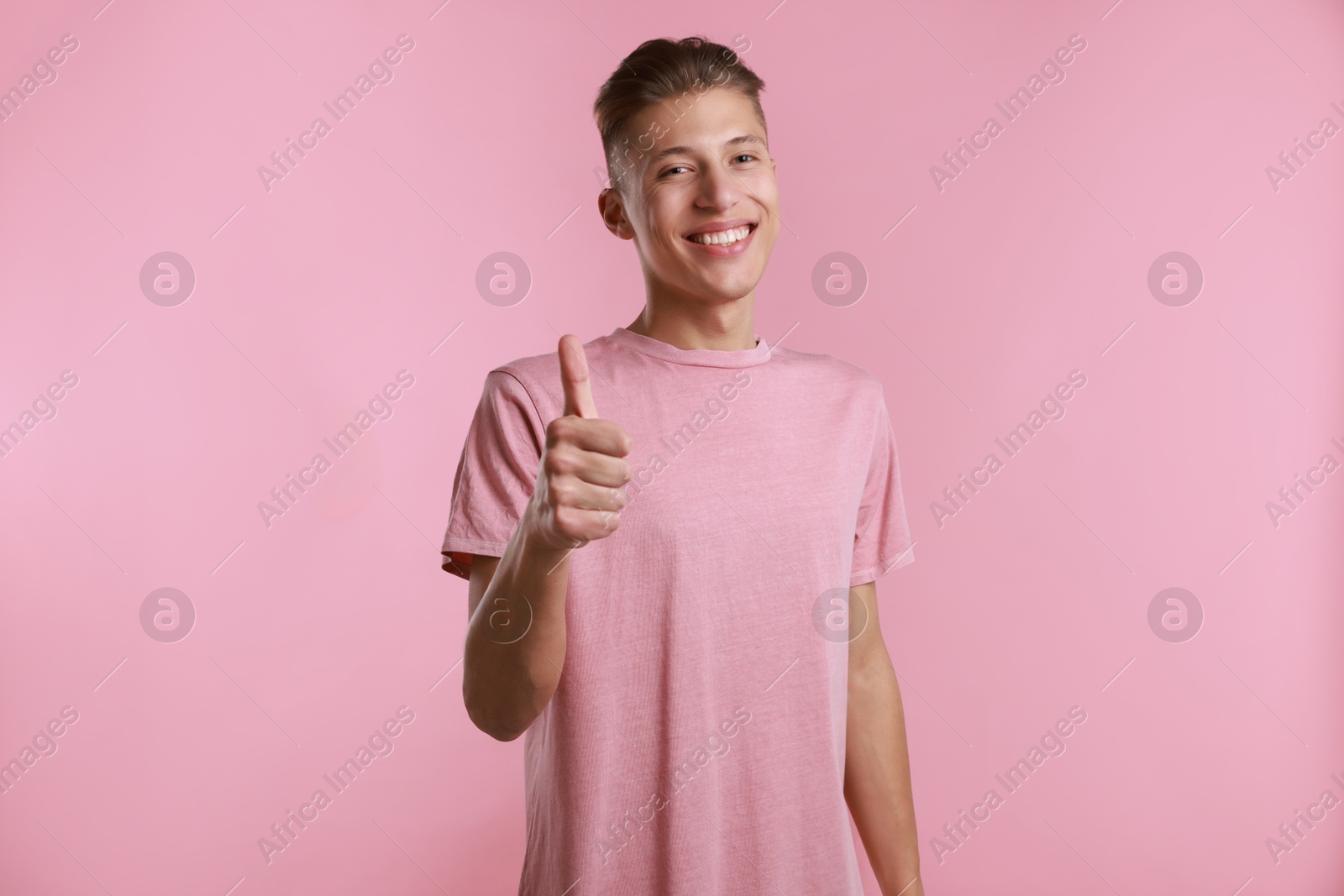 Photo of Happy man showing thumbs up on pink background. Like gesture