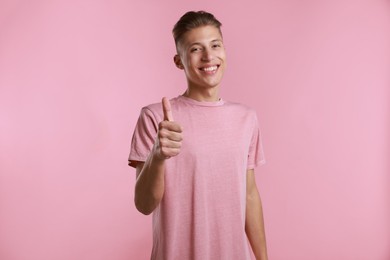 Photo of Happy man showing thumbs up on pink background. Like gesture