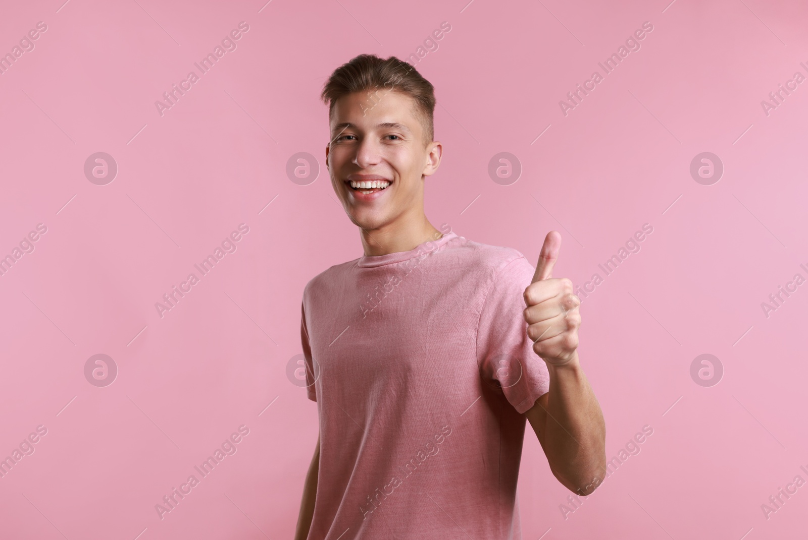 Photo of Happy man showing thumbs up on pink background. Like gesture