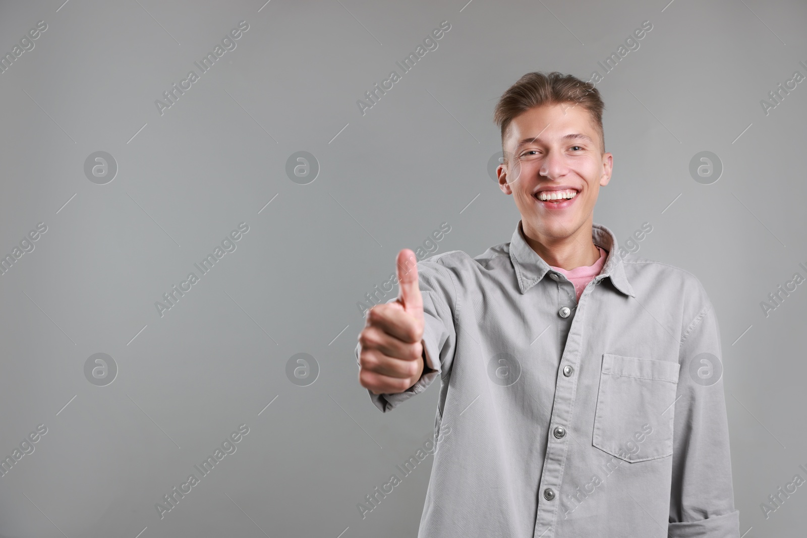 Photo of Happy man showing thumbs up on grey background, space for text. Like gesture