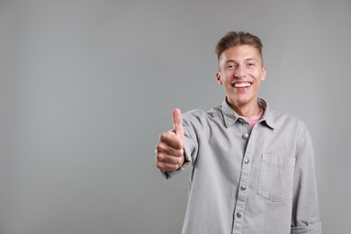 Photo of Happy man showing thumbs up on grey background, space for text. Like gesture