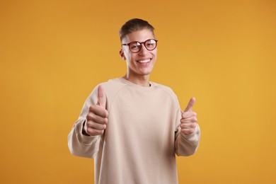 Photo of Happy man showing thumbs up on orange background. Like gesture