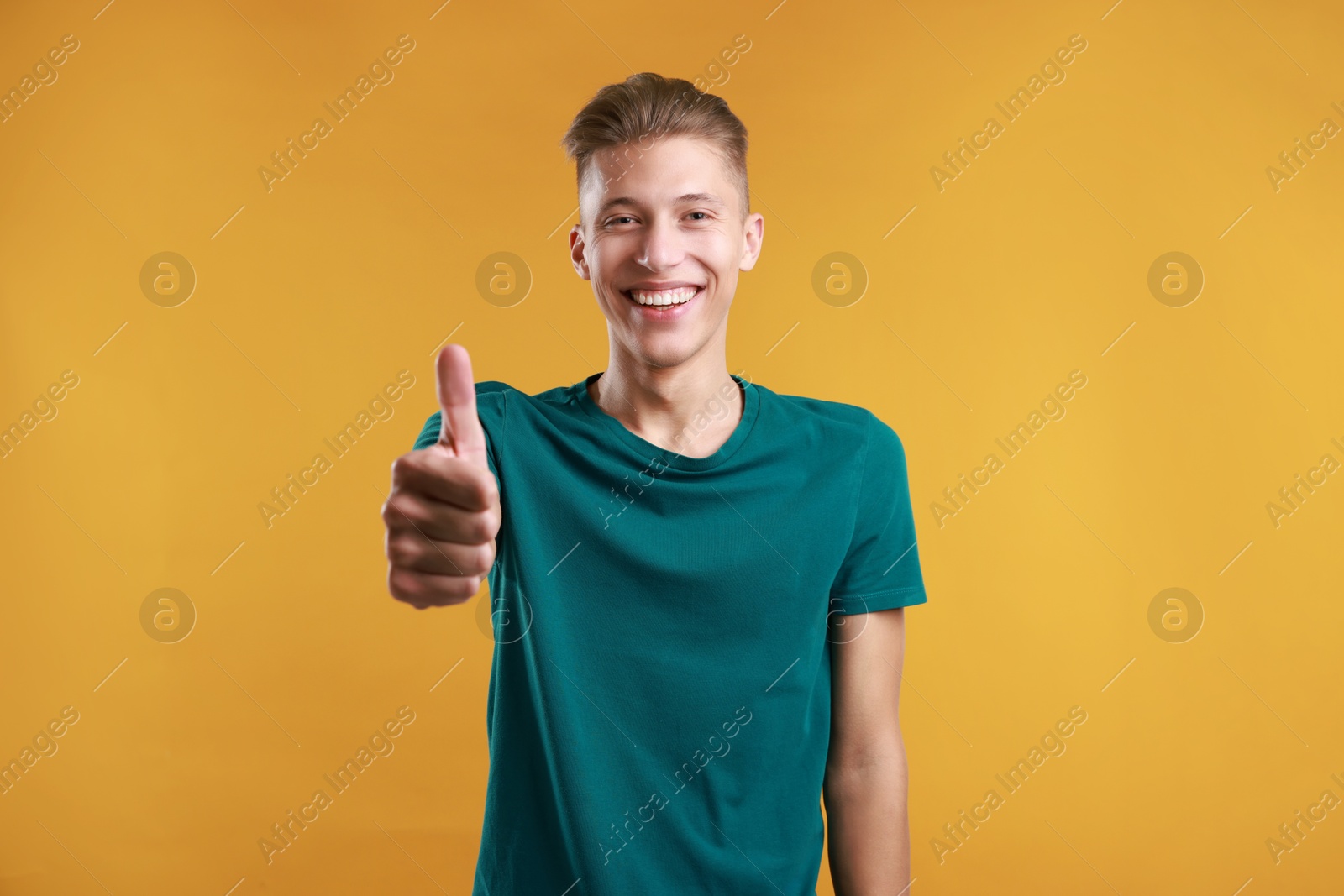 Photo of Happy man showing thumbs up on orange background. Like gesture