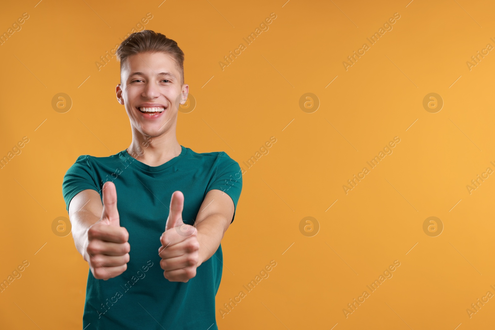 Photo of Happy man showing thumbs up on orange background, space for text. Like gesture