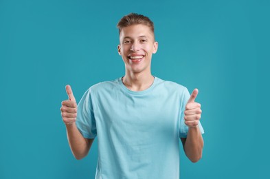 Photo of Happy man showing thumbs up on light blue background. Like gesture