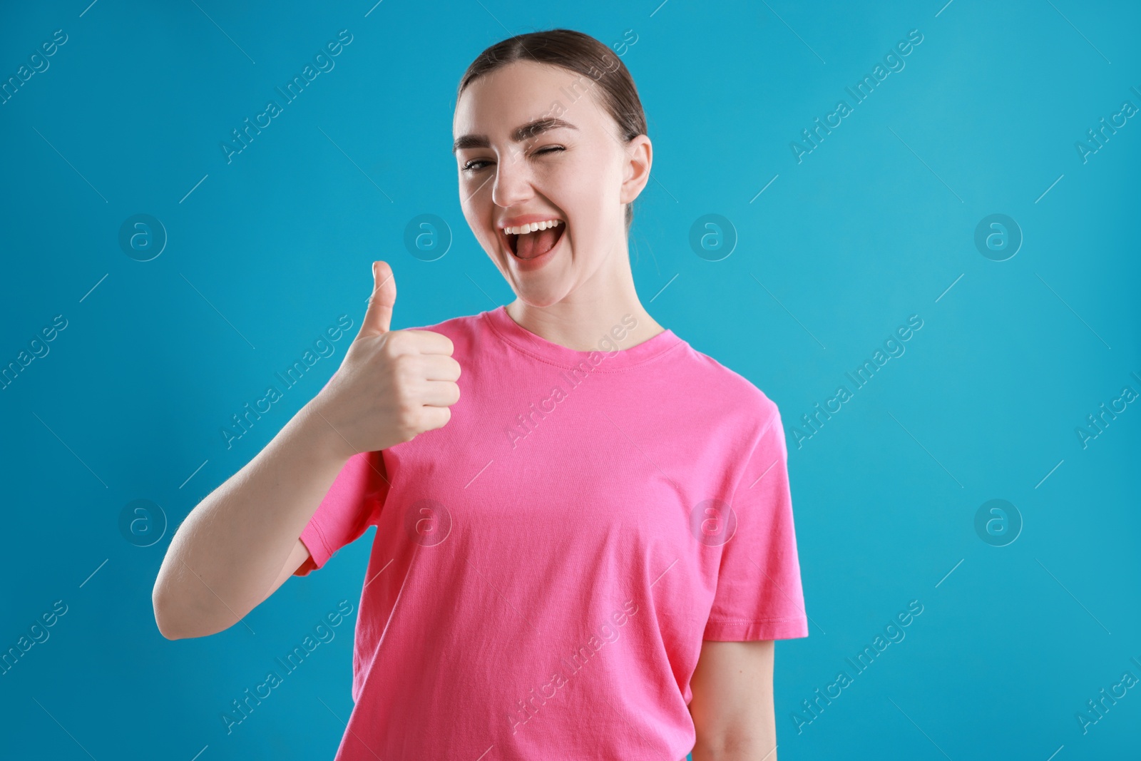 Photo of Happy woman showing thumbs up on light blue background. Like gesture