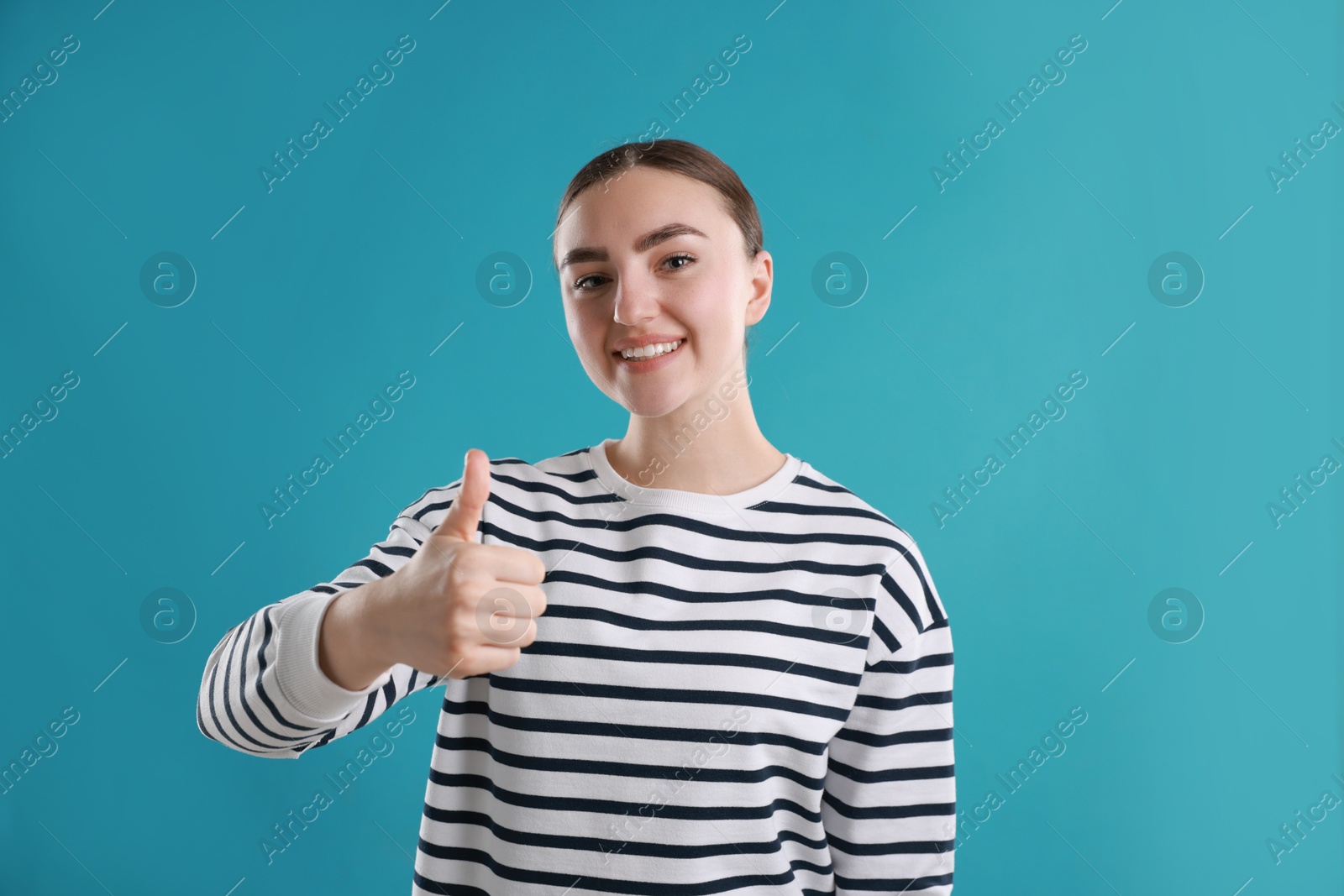 Photo of Happy woman showing thumbs up on light blue background. Like gesture