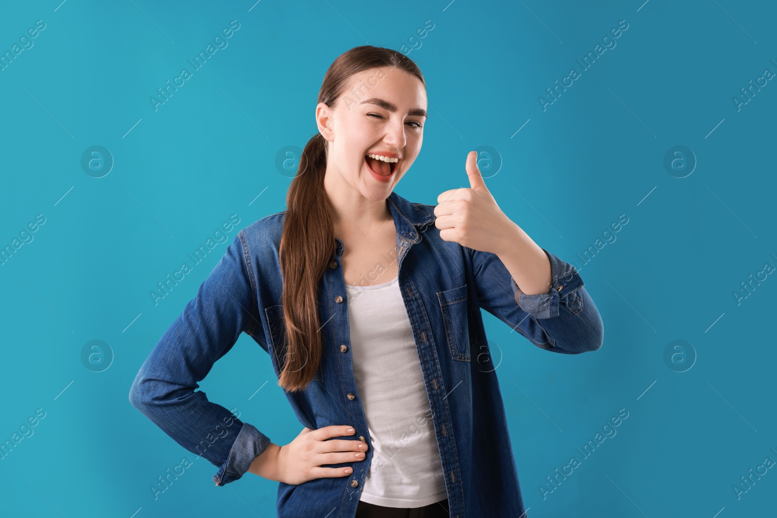 Photo of Happy woman showing thumbs up on light blue background. Like gesture