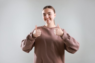 Photo of Happy woman showing thumbs up on grey background. Like gesture