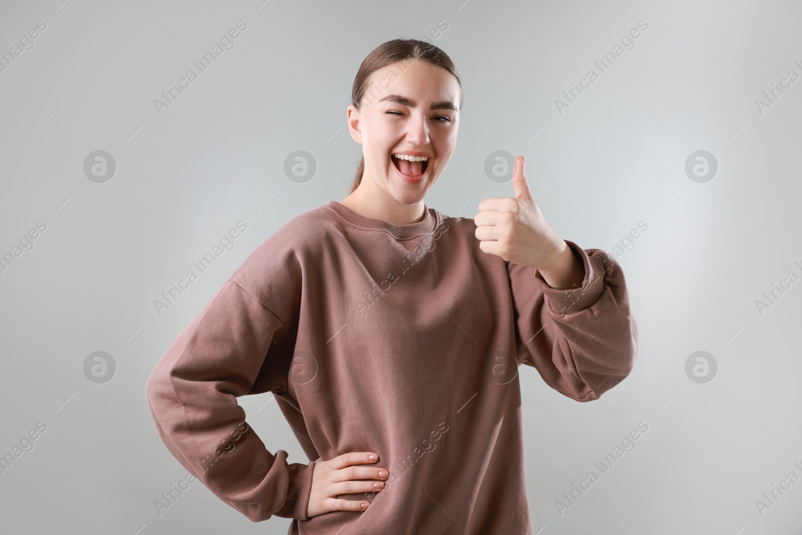 Photo of Happy woman showing thumbs up on grey background. Like gesture