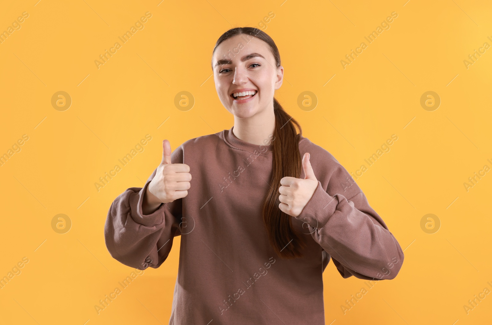 Photo of Happy woman showing thumbs up on yellow background. Like gesture