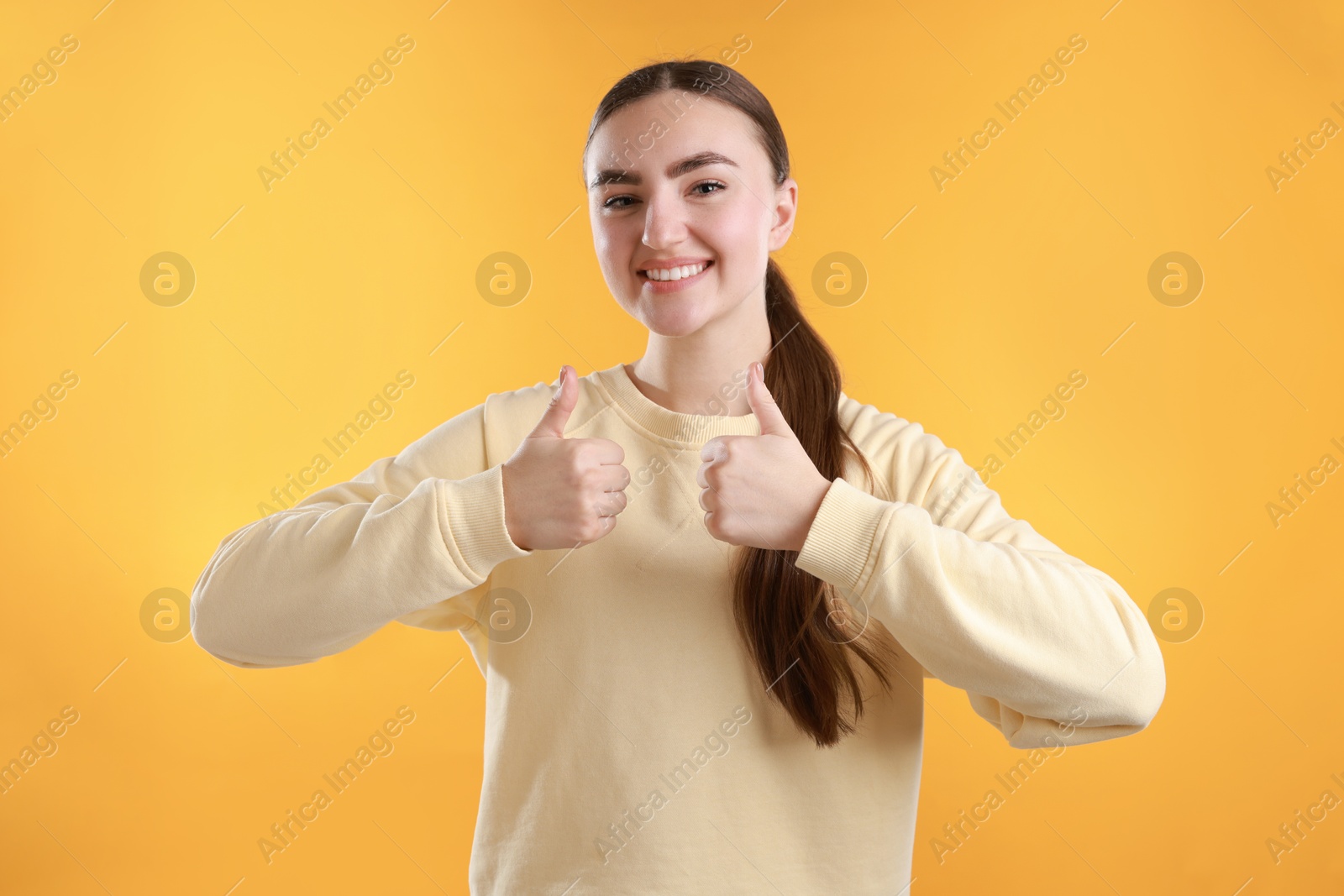 Photo of Happy woman showing thumbs up on yellow background. Like gesture