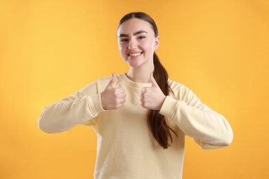 Photo of Happy woman showing thumbs up on yellow background. Like gesture