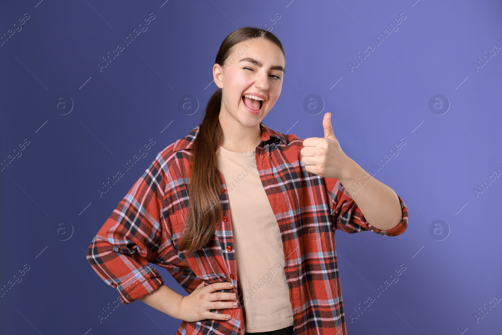 Photo of Happy woman showing thumbs up on purple background. Like gesture