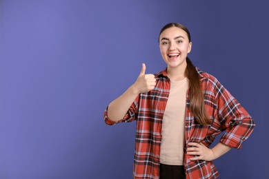 Photo of Happy woman showing thumbs up on purple background, space for text. Like gesture