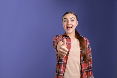 Photo of Happy woman showing thumbs up on purple background, space for text. Like gesture