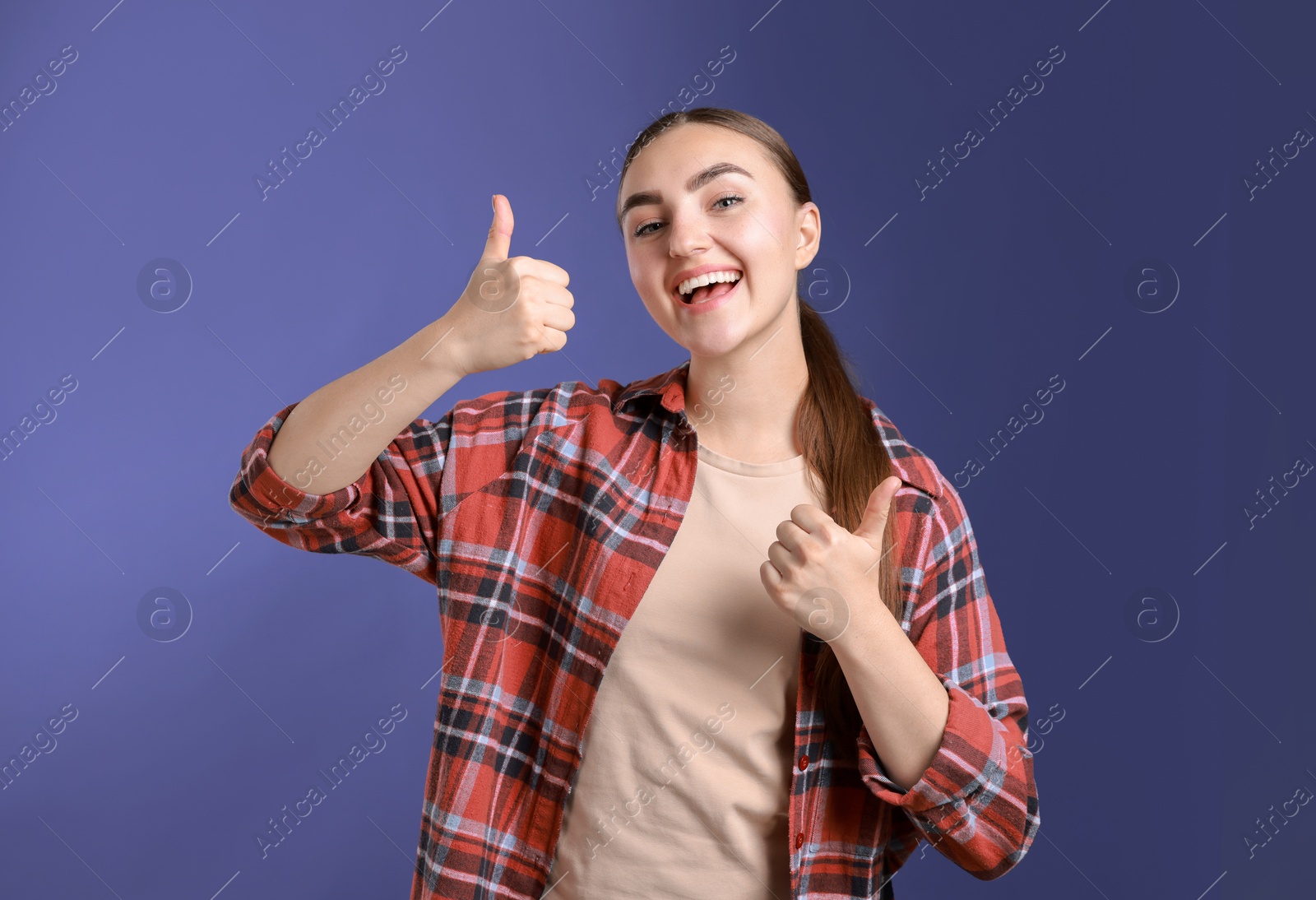 Photo of Happy woman showing thumbs up on purple background. Like gesture