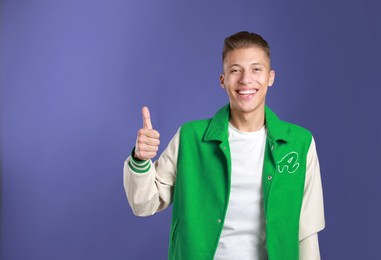 Photo of Happy man showing thumbs up on purple background, space for text. Like gesture