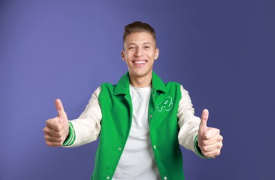 Photo of Happy man showing thumbs up on purple background. Like gesture