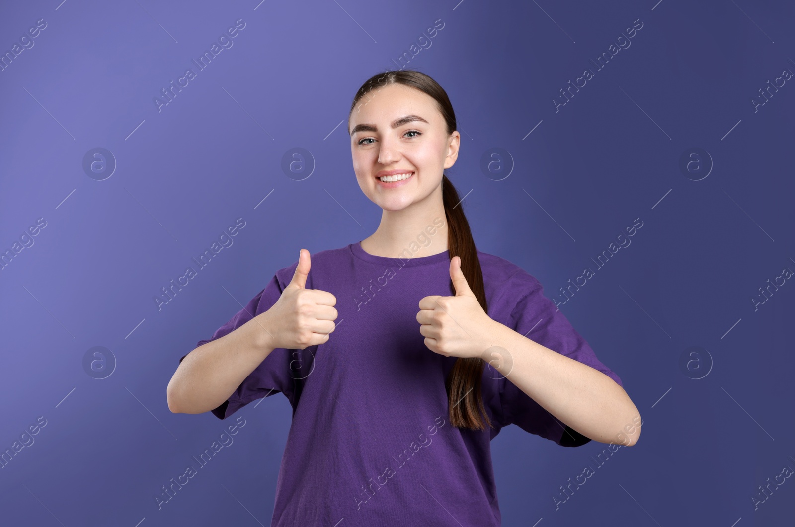 Photo of Happy woman showing thumbs up on purple background. Like gesture