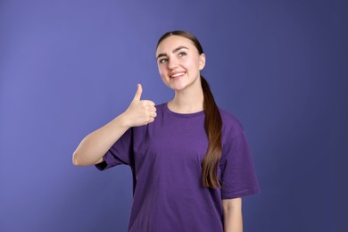 Photo of Happy woman showing thumbs up on purple background. Like gesture