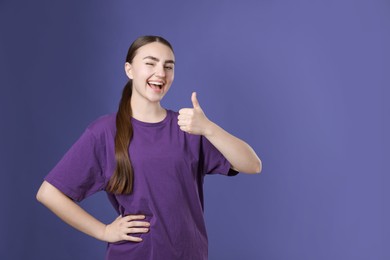 Photo of Happy woman showing thumbs up on purple background, space for text. Like gesture