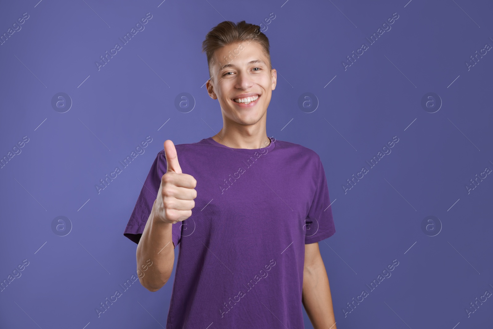 Photo of Happy man showing thumbs up on purple background. Like gesture