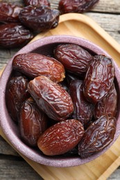 Photo of Many tasty dried dates in bowl on wooden table, top view